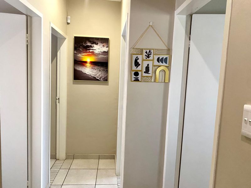 A clean, neutral-toned hallway featuring tiled flooring and multiple doorways leading to adjacent rooms.