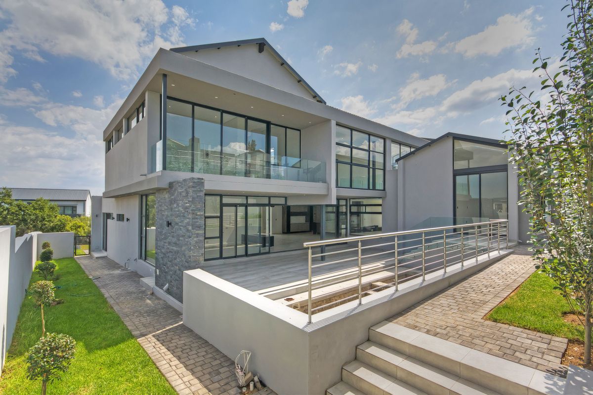 Modern double-story rear elevation featuring extensive glass sliding doors, a spacious paved patio, stone cladding accents, and contemporary glass balustrades.