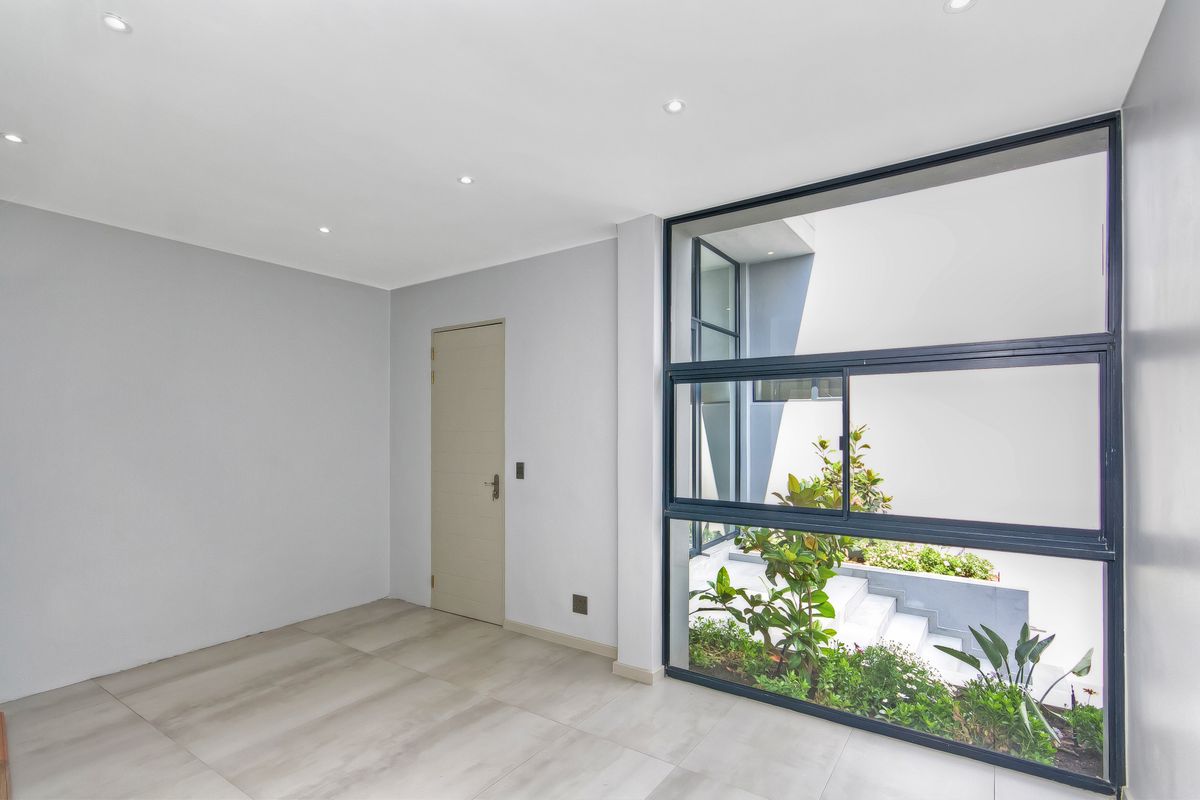 A bright, modern, and empty living space featuring large aluminium-framed windows that provide a view of the outdoor garden area.