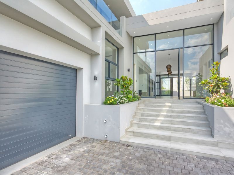 Modern architectural front entrance featuring a large glass facade, concrete staircase, paved driveway, and integrated garage with a sleek sectional door.