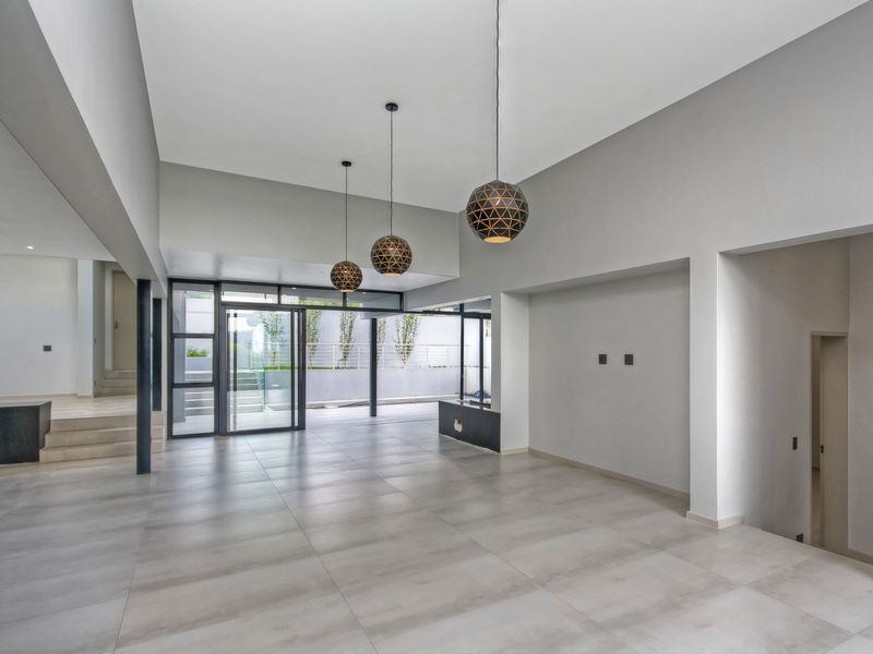 Spacious, modern open-plan living area featuring large format floor tiles, high ceilings, contemporary pendant lighting, and seamless access to the outdoor space.