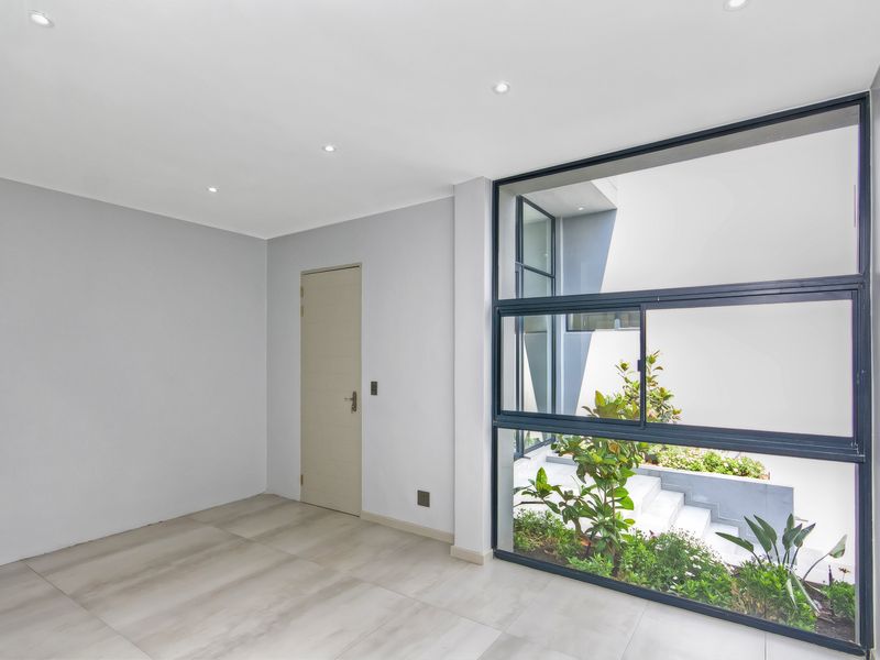 A bright, modern, and empty living space featuring large aluminium-framed windows that provide a view of the outdoor garden area.