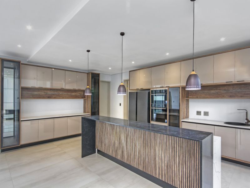 Modern kitchen featuring sleek cabinetry, a central island with stone countertop, integrated appliances, and contemporary pendant lighting in a clean, open-plan layout.