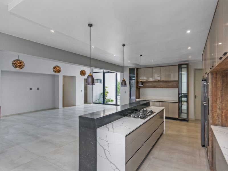 Modern open-plan kitchen and living area featuring a large stone-topped island with integrated gas cooktop, sleek cabinetry, and expansive sliding glass doors.