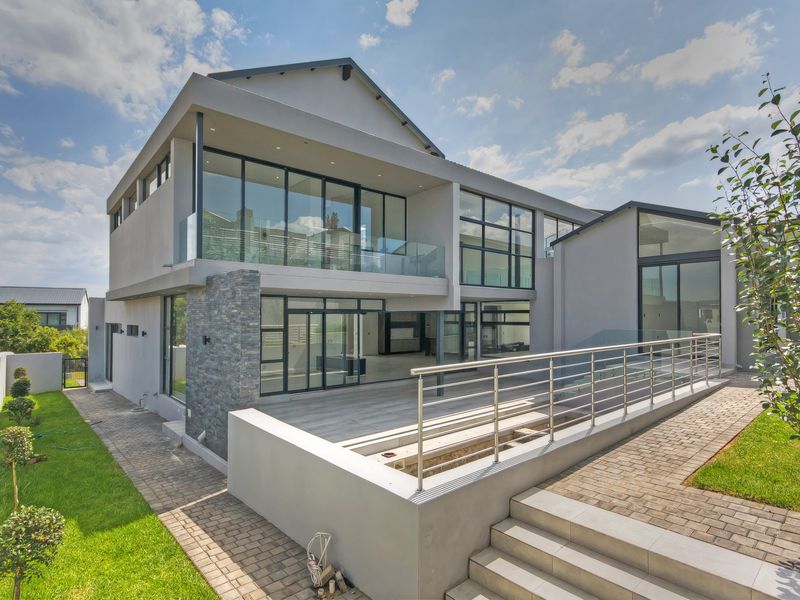 Modern double-story rear elevation featuring extensive glass sliding doors, a spacious paved patio, stone cladding accents, and contemporary glass balustrades.