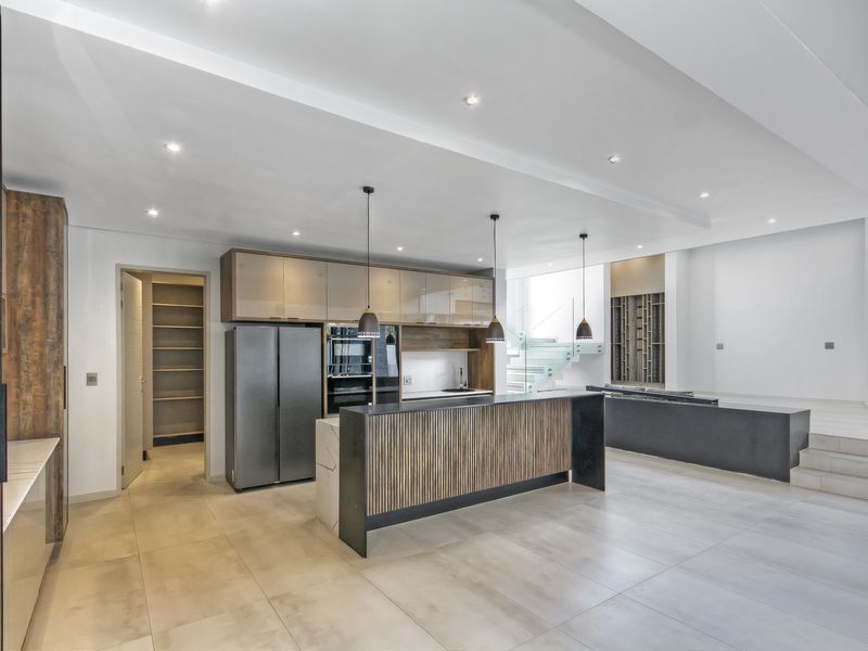 Modern open-plan kitchen featuring a large island, sleek cabinetry, integrated appliances, and a walk-in pantry, finished with high-quality tiling and contemporary lighting.