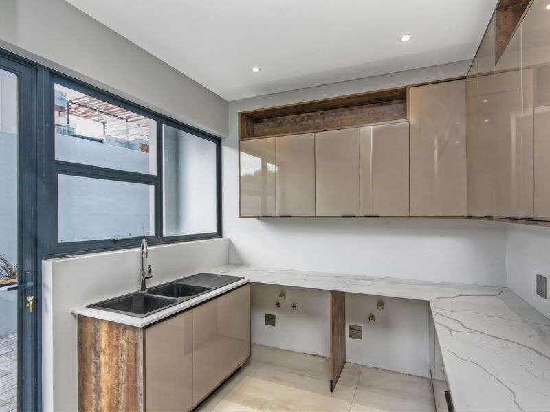 A modern, well-appointed scullery featuring sleek cabinetry, stone countertops, a double basin sink, and dedicated plumbing connections for appliances.
