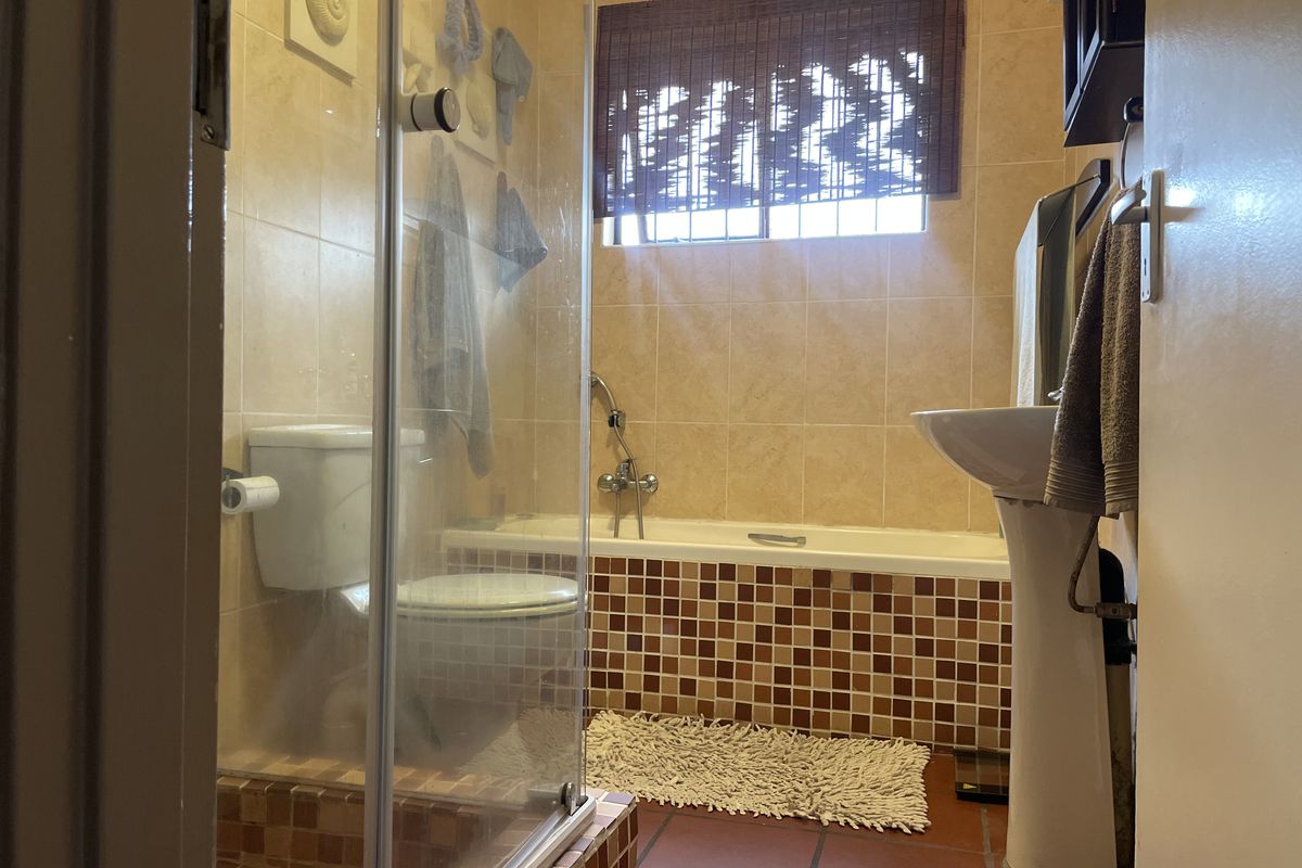 A functional bathroom featuring a pedestal basin, bathtub, and a separate glass-enclosed shower with mosaic tile detailing.