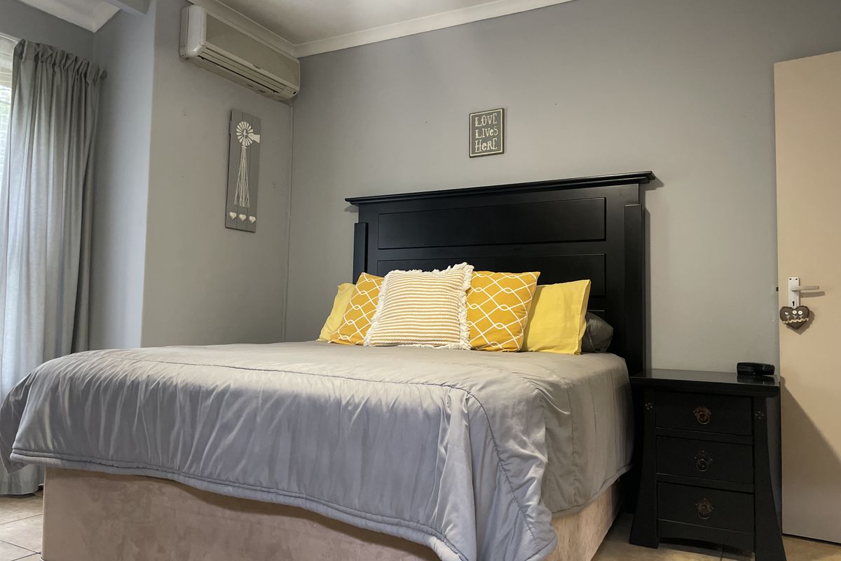 A bedroom featuring tiled flooring, a wall-mounted split-system air conditioner, and neutral grey wall finishes.