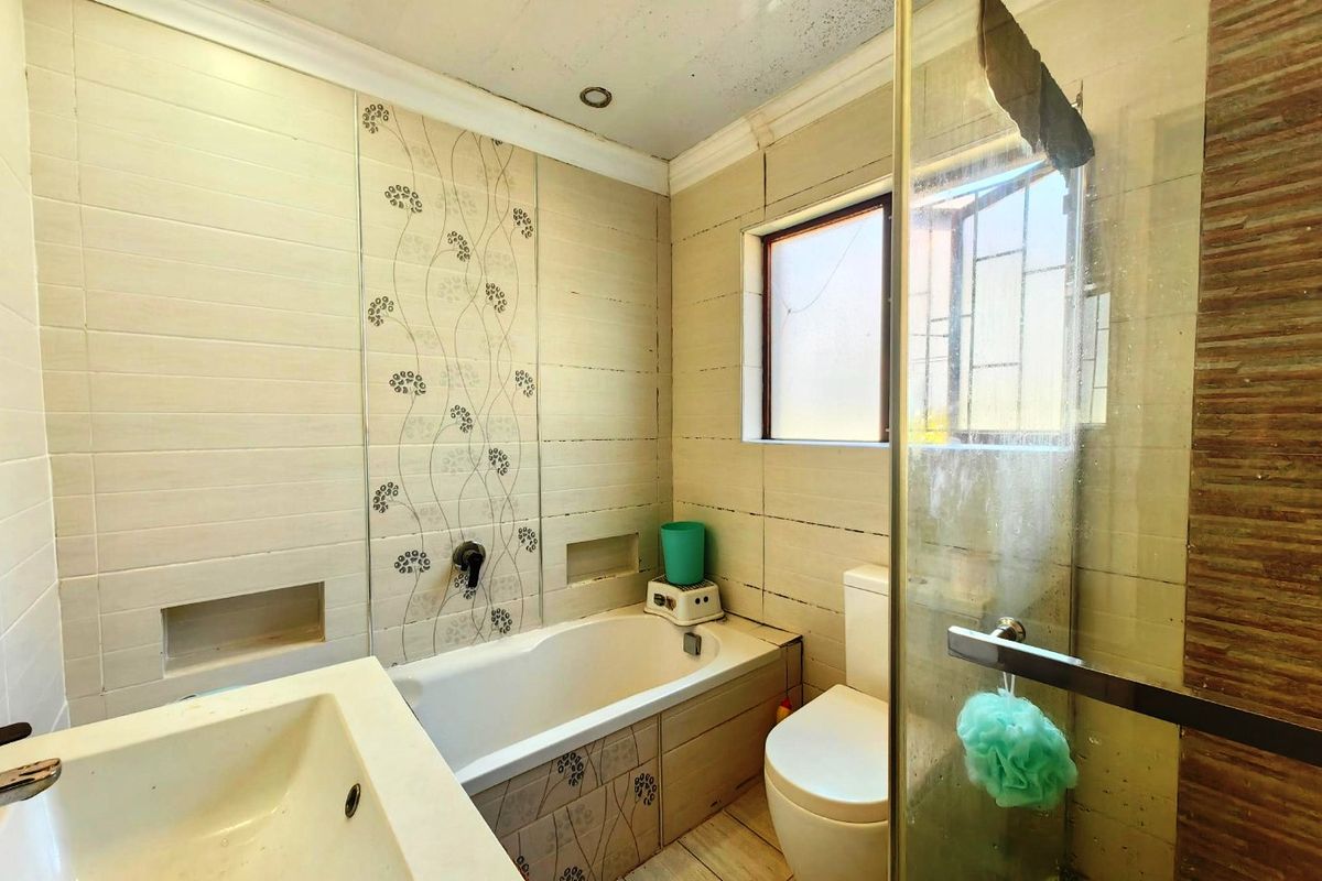 A functional bathroom featuring a built-in bathtub, separate glass shower enclosure, wall-mounted toilet, and vanity basin with tiled finishes throughout.
