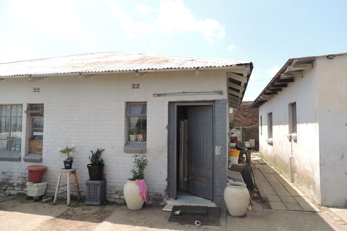 Rear view of a residential property featuring a corrugated metal roof, brick exterior walls, and a paved side walkway.