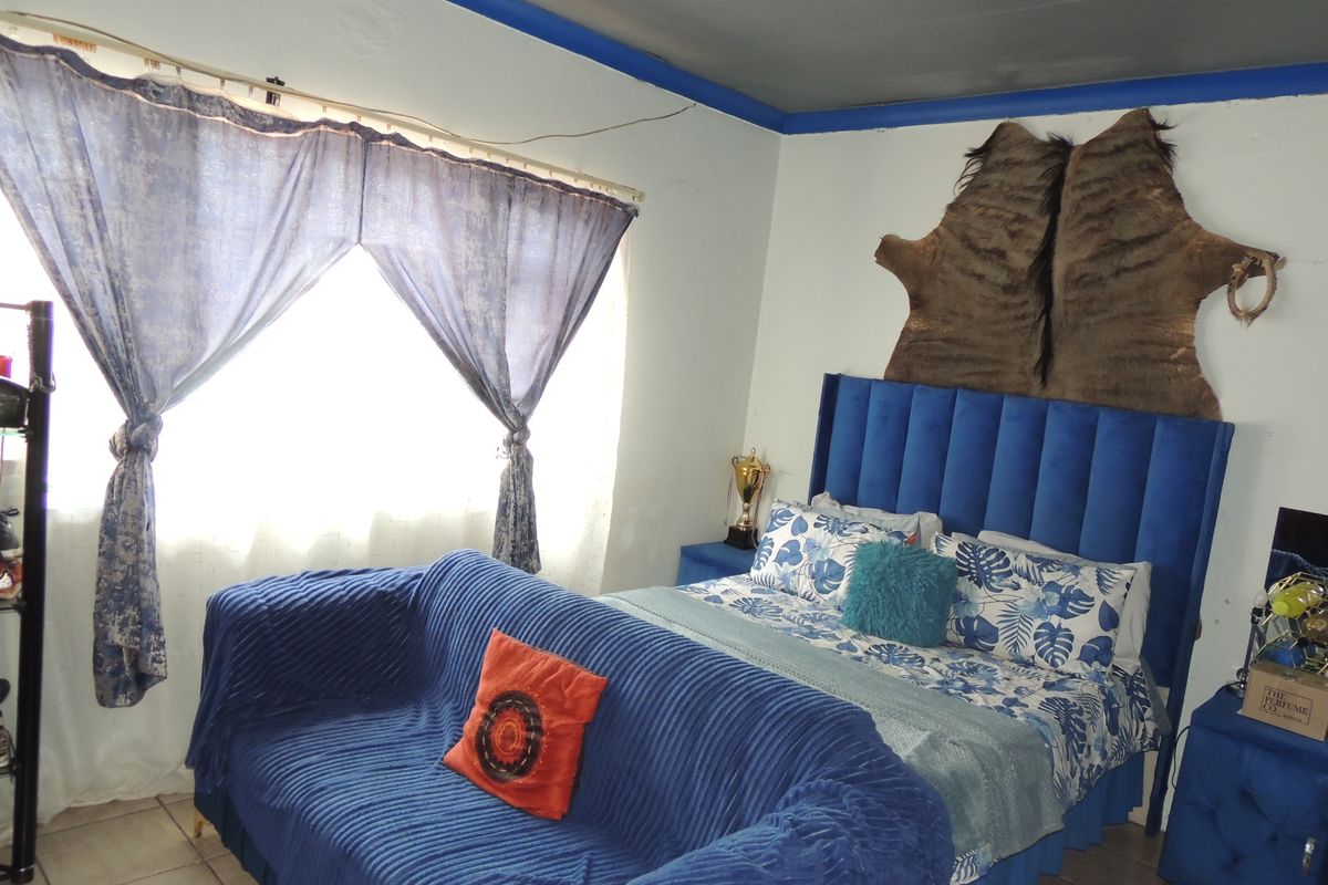 A bedroom featuring tiled flooring and painted walls, currently styled with a blue upholstered bed frame and matching decor.