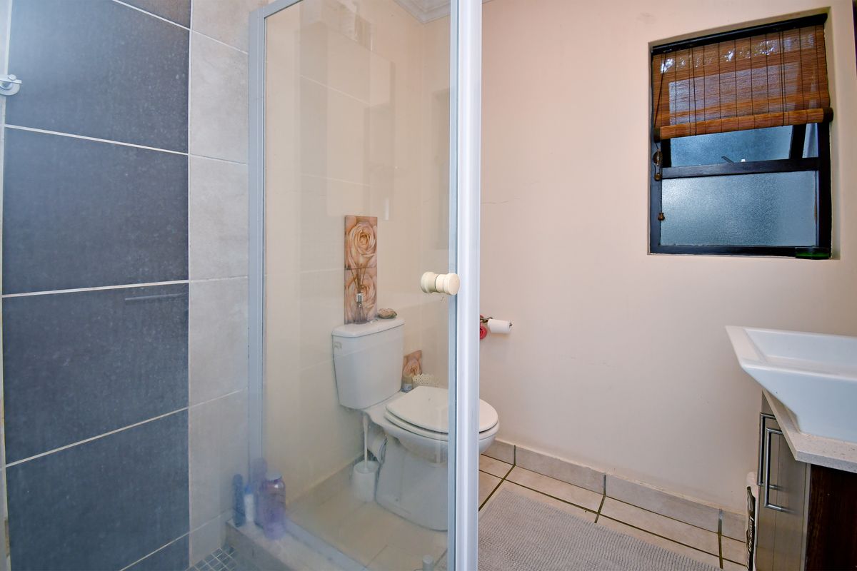 A functional bathroom featuring a glass-enclosed shower, a wall-mounted basin, and a toilet, finished with neutral wall tiles and floor tiling.