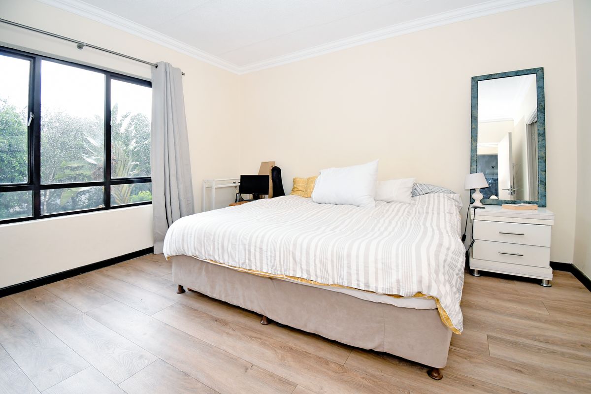 A well-lit bedroom featuring light wood-look flooring, large windows with natural light, and crown molding.