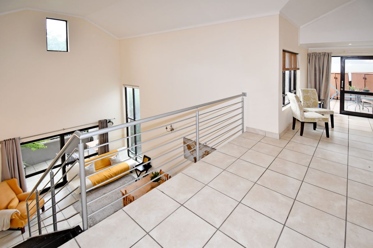 A bright mezzanine level overlooking the living area, featuring tiled flooring, a modern metal balustrade, and access to an outdoor balcony.