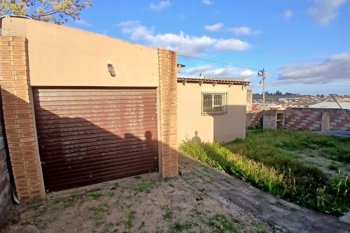 Rear exterior view of the property featuring a roller garage door, brick masonry walls, security bars on windows, and an outdoor braai area.