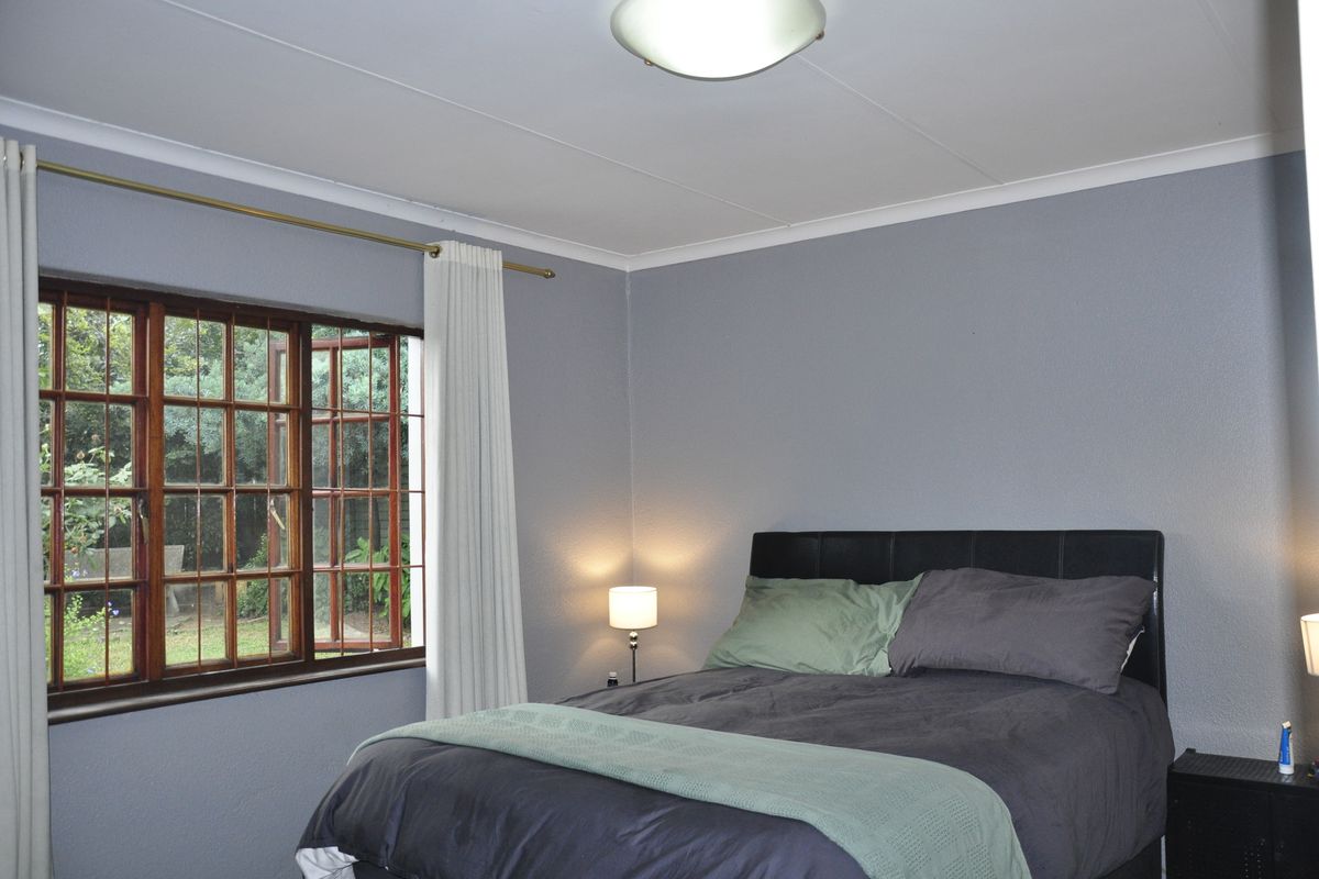 A bedroom featuring timber-framed casement windows with security bars, overlooking a garden area.