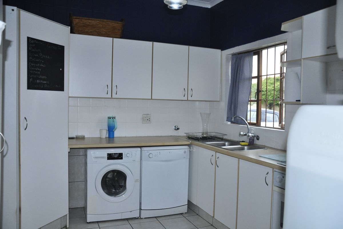 A functional kitchen featuring white cabinetry, tiled splashbacks, double stainless steel sink, and dedicated under-counter space for laundry and dishwasher appliances.