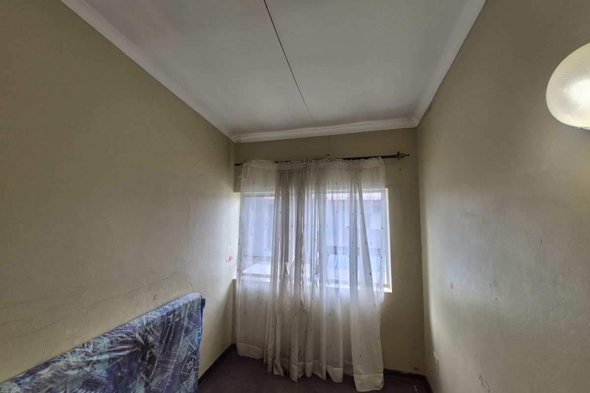 A compact bedroom featuring a window with natural light, neutral wall tones, and carpeted flooring.