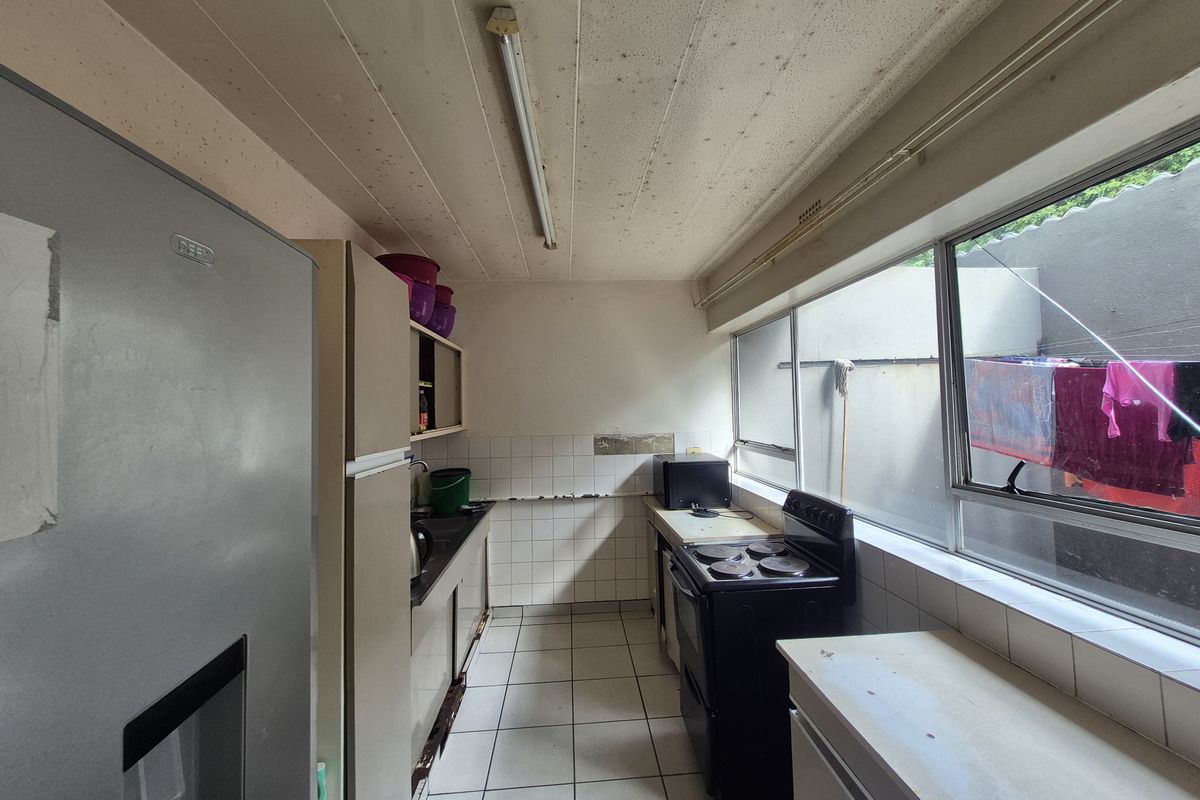 A functional galley-style kitchen featuring tiled flooring, tiled splashbacks, and large windows providing natural light and views of the rear exterior area.