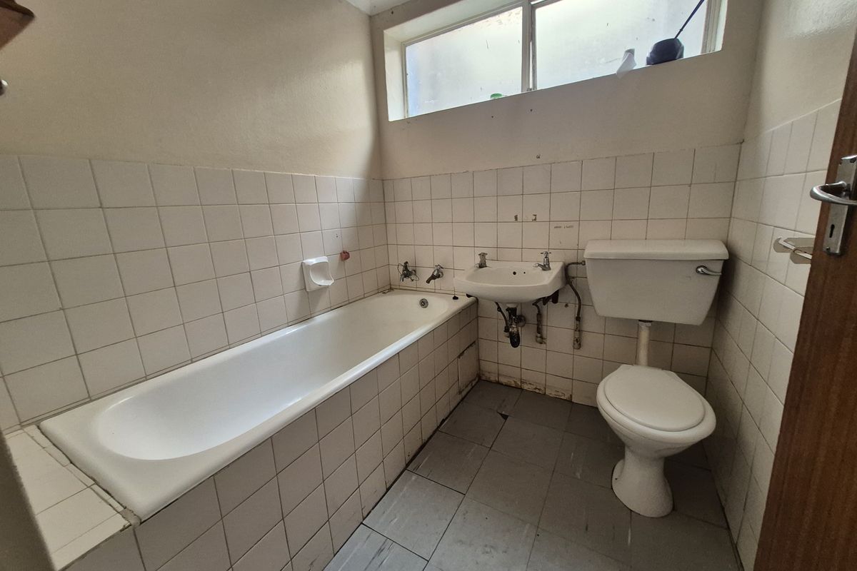 A dated bathroom featuring a standard bathtub, wall-mounted basin, and toilet with tiled walls and flooring, requiring modernization and cosmetic updates.