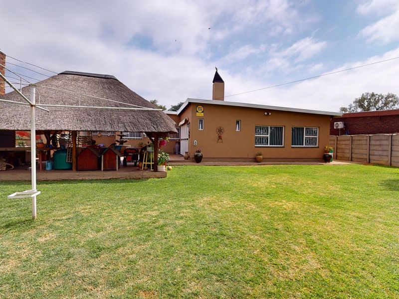 Rear view of the property featuring a spacious lawn, a thatched lapa entertainment area, and a secure boundary wall.