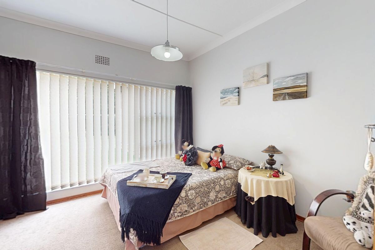 A bedroom featuring carpet flooring, a pendant light fixture, and large windows fitted with vertical blinds.