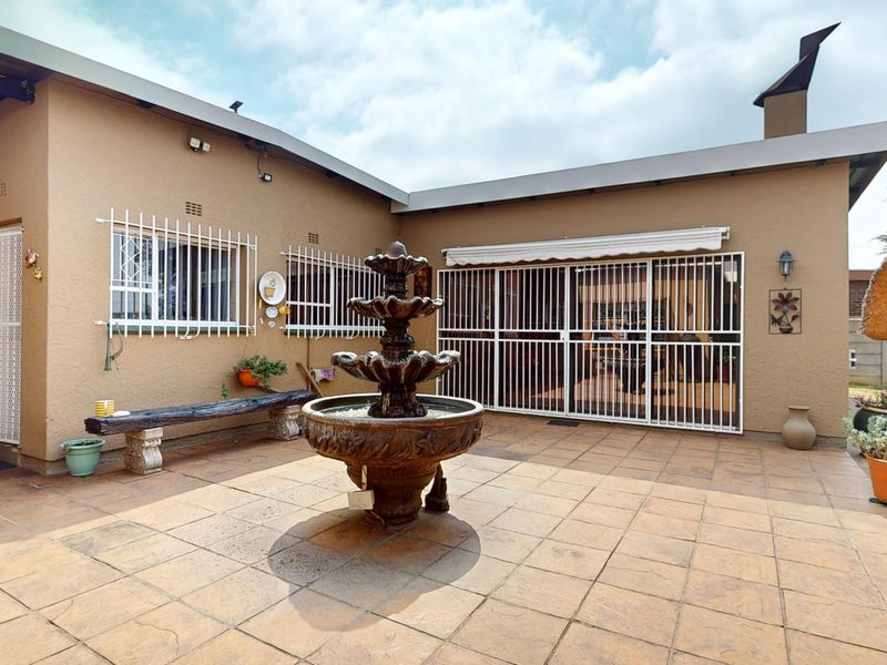 A paved rear patio area featuring a central water fountain, security gates, and a retractable awning attached to the main building structure.