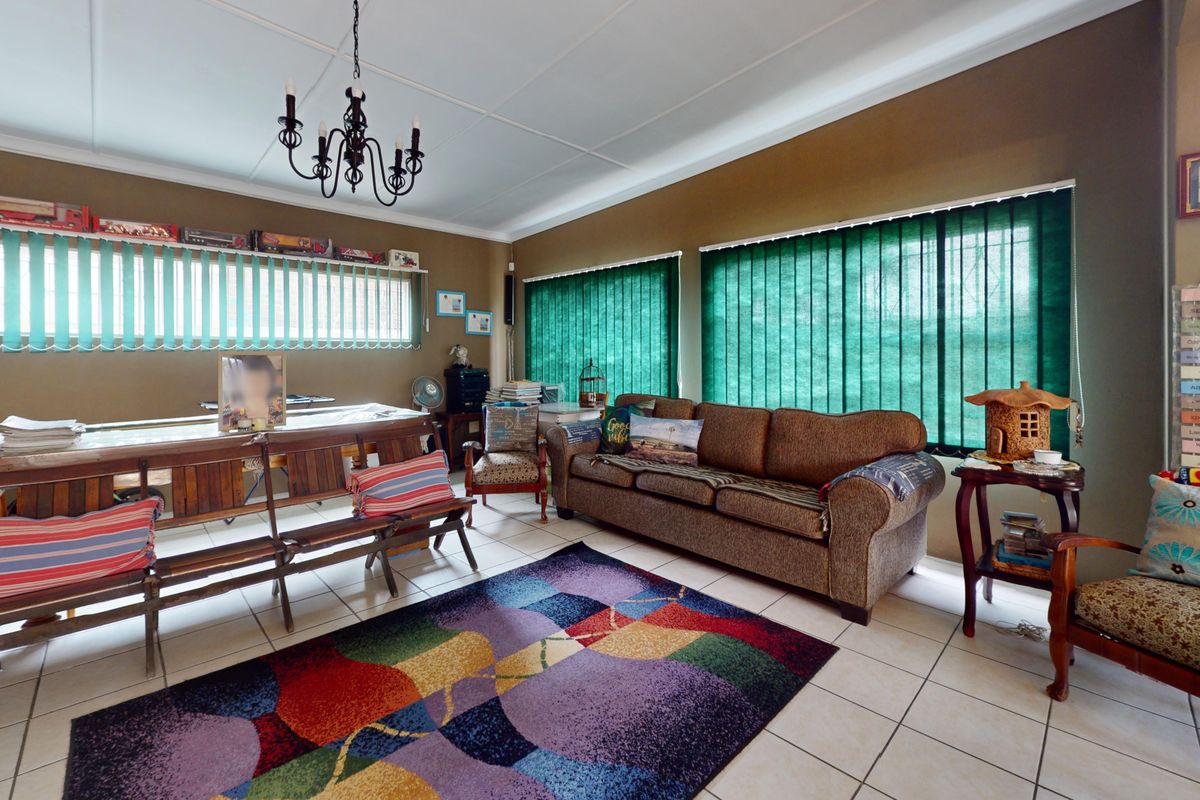 A spacious living room featuring tiled flooring, large windows with vertical blinds, and a central ceiling light fixture.