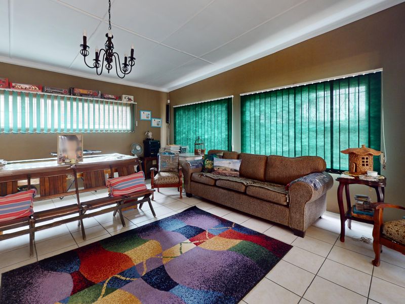 A spacious living room featuring tiled flooring, large windows with vertical blinds, and a central ceiling light fixture.
