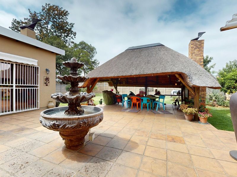Spacious outdoor patio area featuring a traditional thatched lapa with a built-in brick fireplace and a decorative stone water fountain.