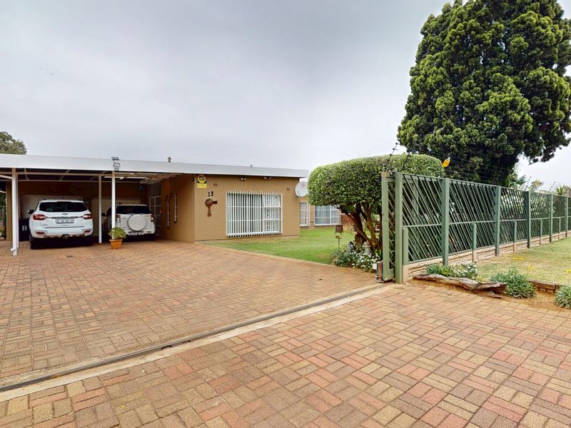 Front exterior view of the property featuring a paved driveway, covered carport, and secure perimeter fencing with an integrated gate.