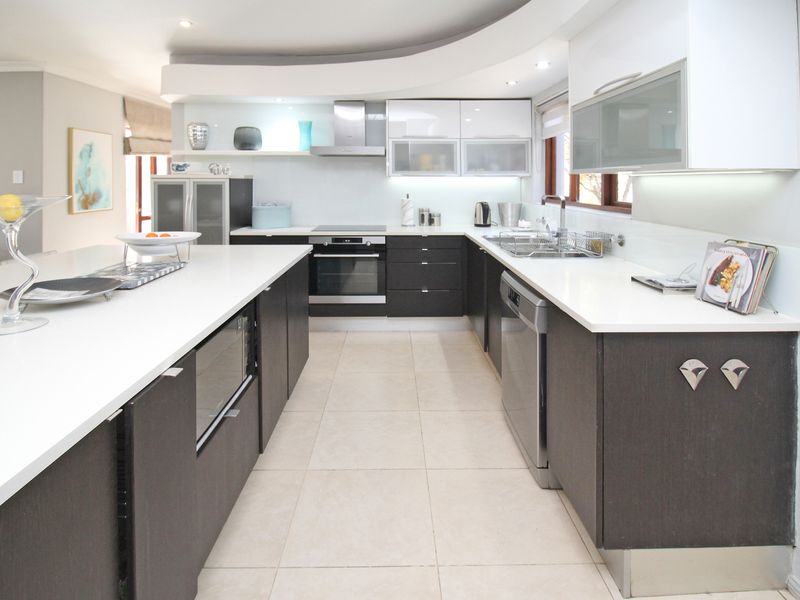 Modern kitchen featuring a large central island, dark cabinetry, white stone countertops, integrated appliances, and recessed ceiling lighting.