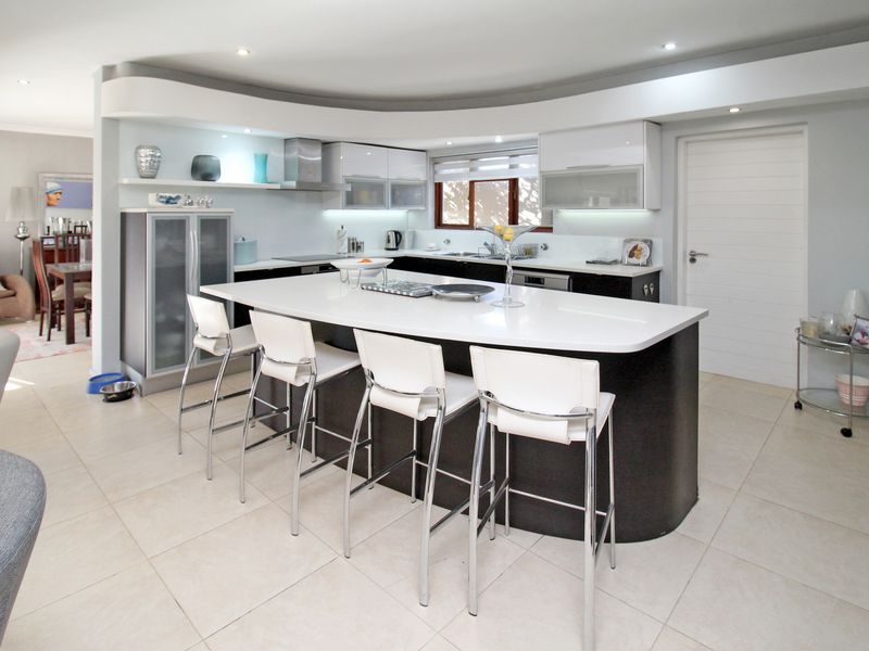Modern open-plan kitchen featuring a large curved island with quartz countertops, high-gloss cabinetry, and integrated lighting, seamlessly flowing into the adjacent living area.
