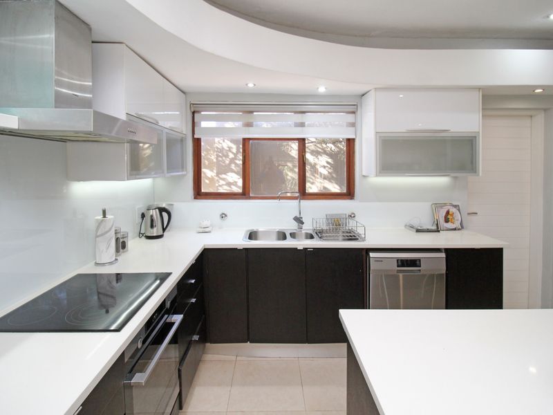 Modern kitchen featuring high-gloss cabinetry, stone countertops, integrated appliances, and a sleek electric cooktop with a stainless steel extractor fan.
