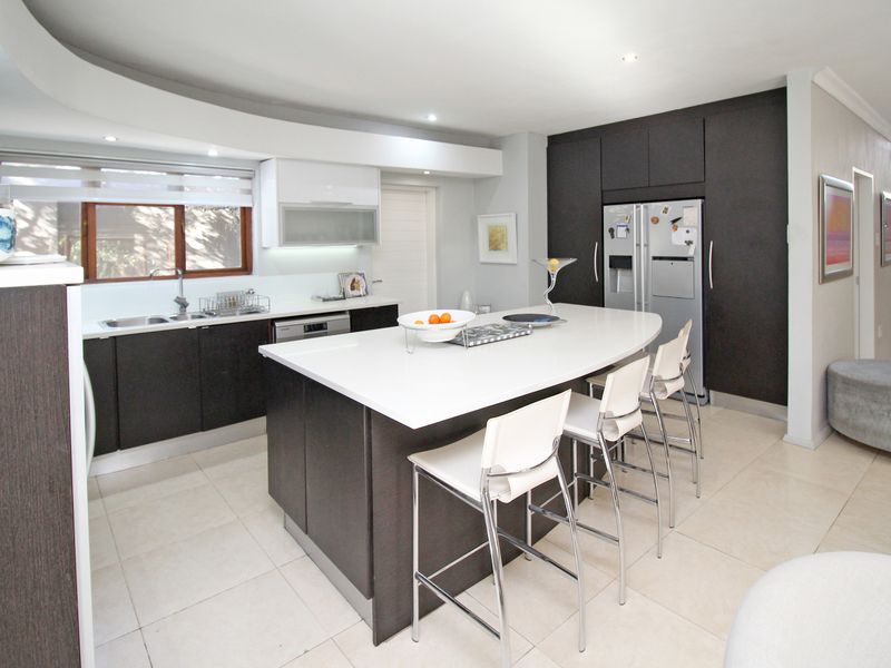 Modern kitchen featuring a large central island with breakfast bar seating, sleek dark cabinetry, integrated appliances, and bright tiled flooring.