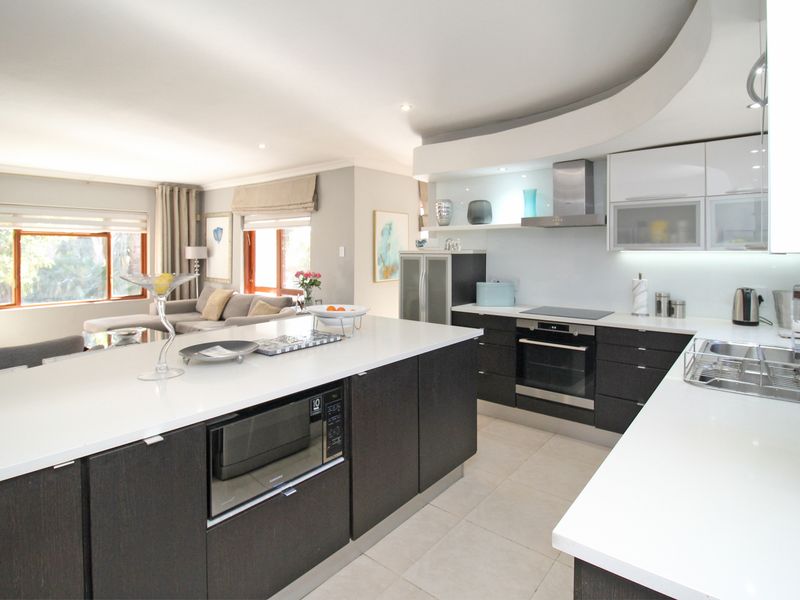 Modern open-plan kitchen featuring a large island, stone countertops, integrated appliances, and recessed lighting, seamlessly flowing into the adjacent living area.
