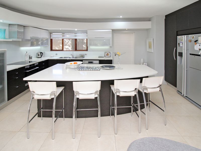 Modern kitchen featuring a large central island, sleek dark and white cabinetry, integrated appliances, and tiled flooring with recessed lighting.