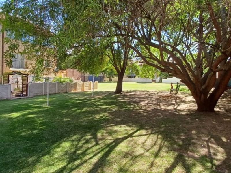 A spacious communal garden area featuring a well-maintained lawn, mature trees, and precast concrete boundary walling, providing a pleasant outdoor space.