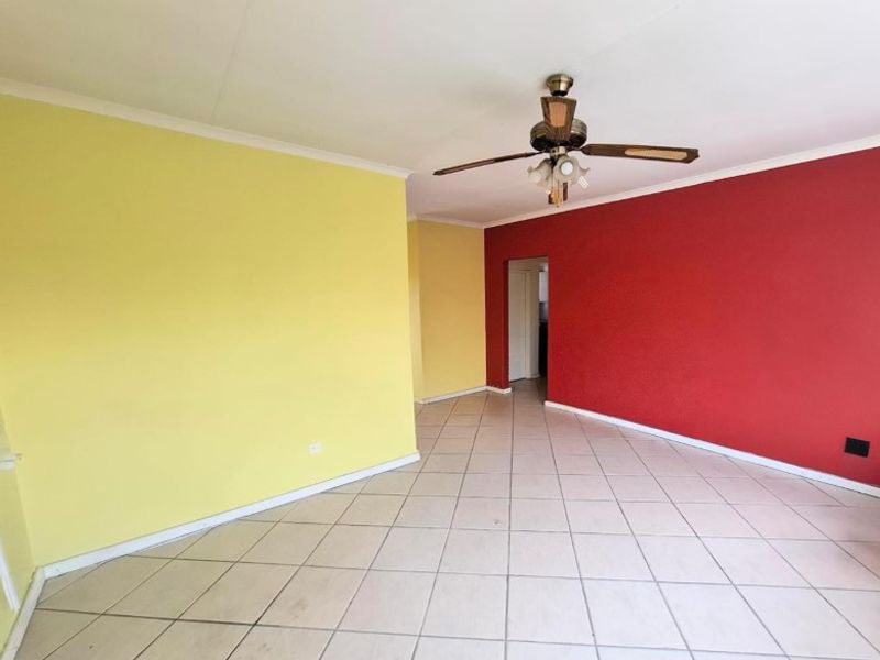 An empty living room featuring ceramic tiled flooring, a ceiling fan, and bold yellow and red accent walls.