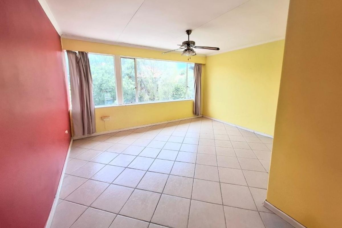 A spacious, empty living room featuring tiled flooring, a ceiling fan, and large windows providing natural light.