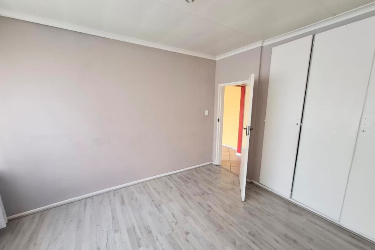 A bright, empty bedroom featuring modern laminate flooring and built-in cupboards, offering a clean and neutral space ready for personalization.