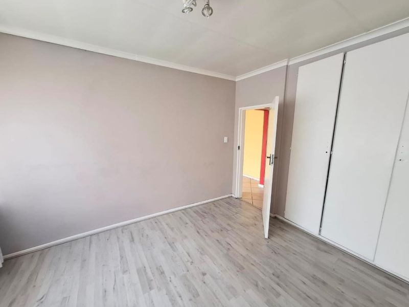 A bright, empty bedroom featuring modern laminate flooring and built-in cupboards, offering a clean and neutral space ready for personalization.