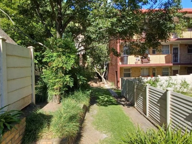 A view of the rear exterior area of the flat complex, featuring a landscaped garden, precast boundary walls, and brick building facades with balconies.