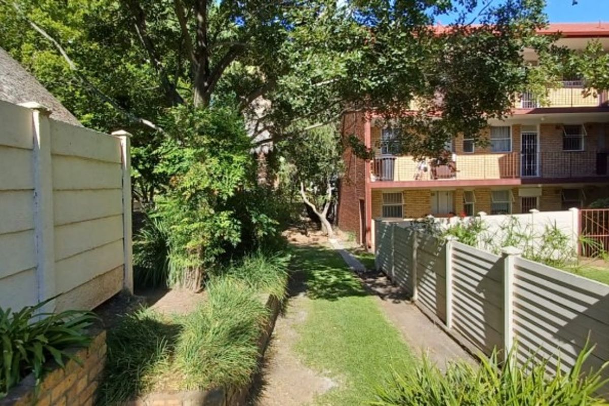 A view of the rear exterior area of the flat complex, featuring a landscaped garden, precast boundary walls, and brick building facades with balconies.