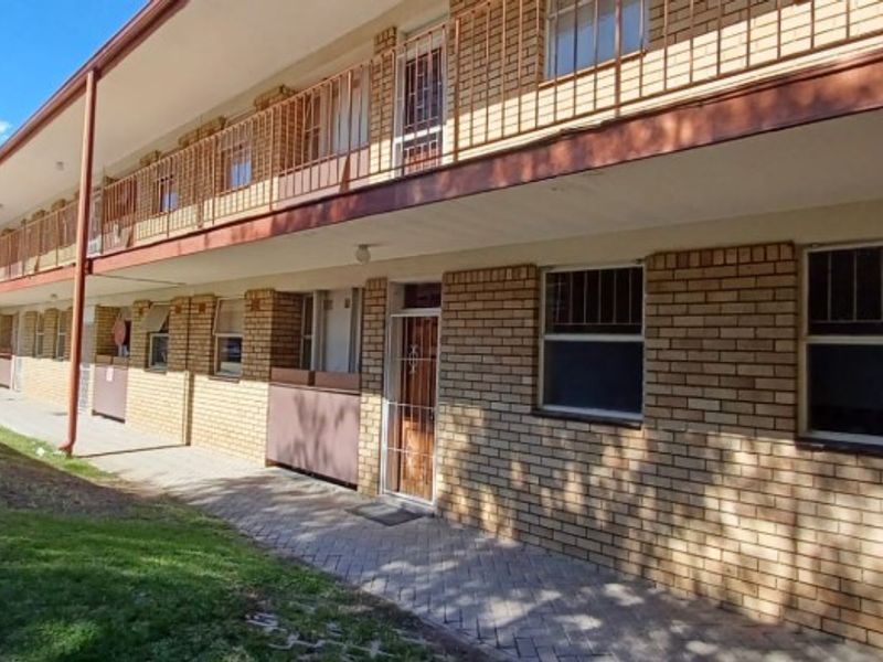 Exterior view of a multi-story flat complex featuring face brick construction, paved walkways, and metal security fixtures on windows and doors.