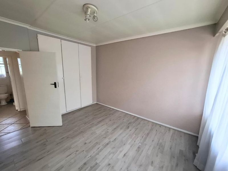 A bright, empty bedroom featuring modern laminate flooring, neutral wall tones, and built-in cupboards, offering a clean canvas for personalization.