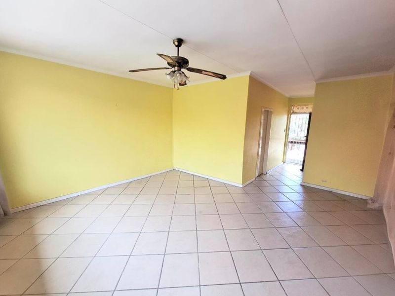 An empty, open-plan living area featuring tiled flooring, a ceiling fan, and a security gate at the entrance.