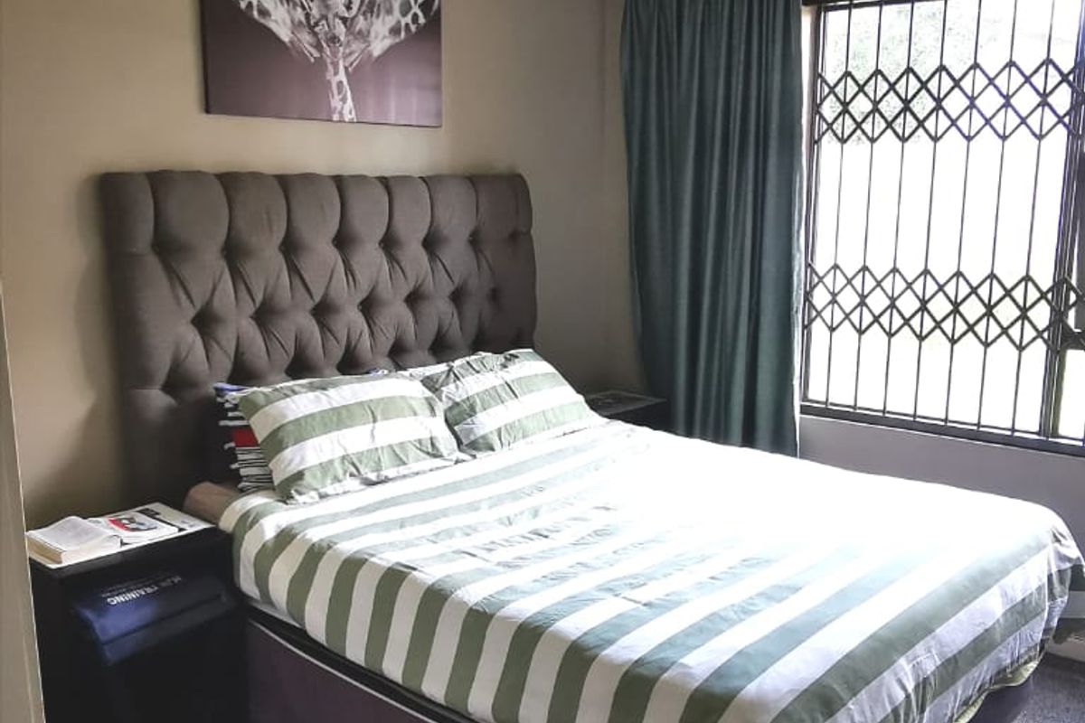 A standard bedroom featuring carpeted flooring, a window with a security gate, and a central ceiling light fixture.
