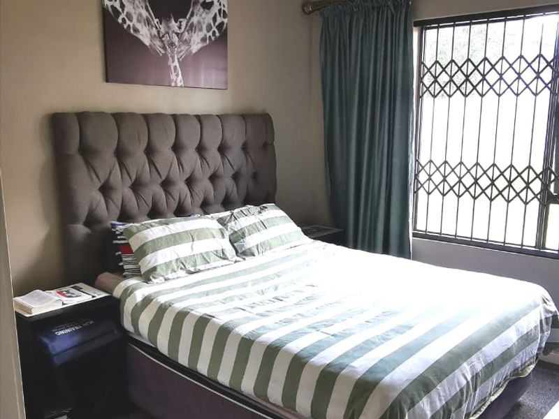 A standard bedroom featuring carpeted flooring, a window with a security gate, and a central ceiling light fixture.